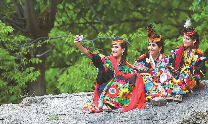 A Kalash woman wearing a traditional dress takes a selfie with her friends during a break as they celebrate ‘Joshi’, a festival to welcome the arrival of spring