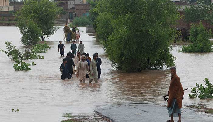 Residents wade through a flooded road, following the monsoon rains and rising water level of the Chenab River, in Patraki, Chiniot district of the Punjab